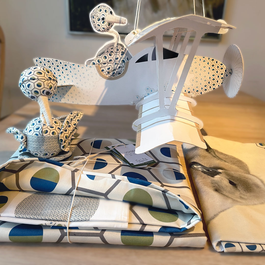 Image showing adult bedding and baby bedding. A bird made of fabric from the adult bedding kit and in the background a cardboard plane with a image of the bird.